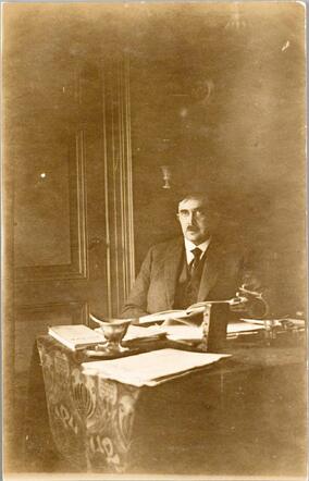 De heer J.M. Boas, makelaar, zittend op een stoel aan een tafel, 1923.